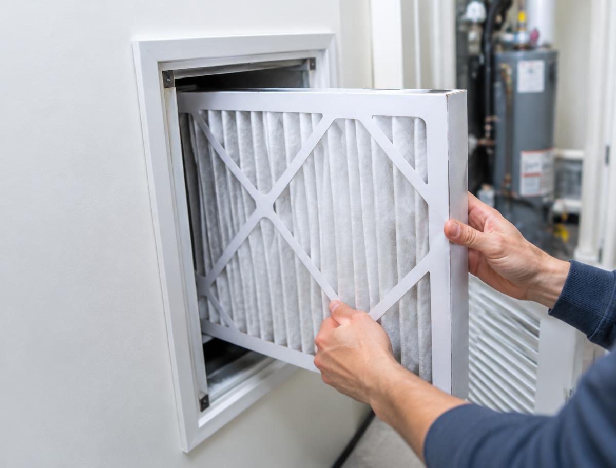 Hands sliding a new air filter into a return vent